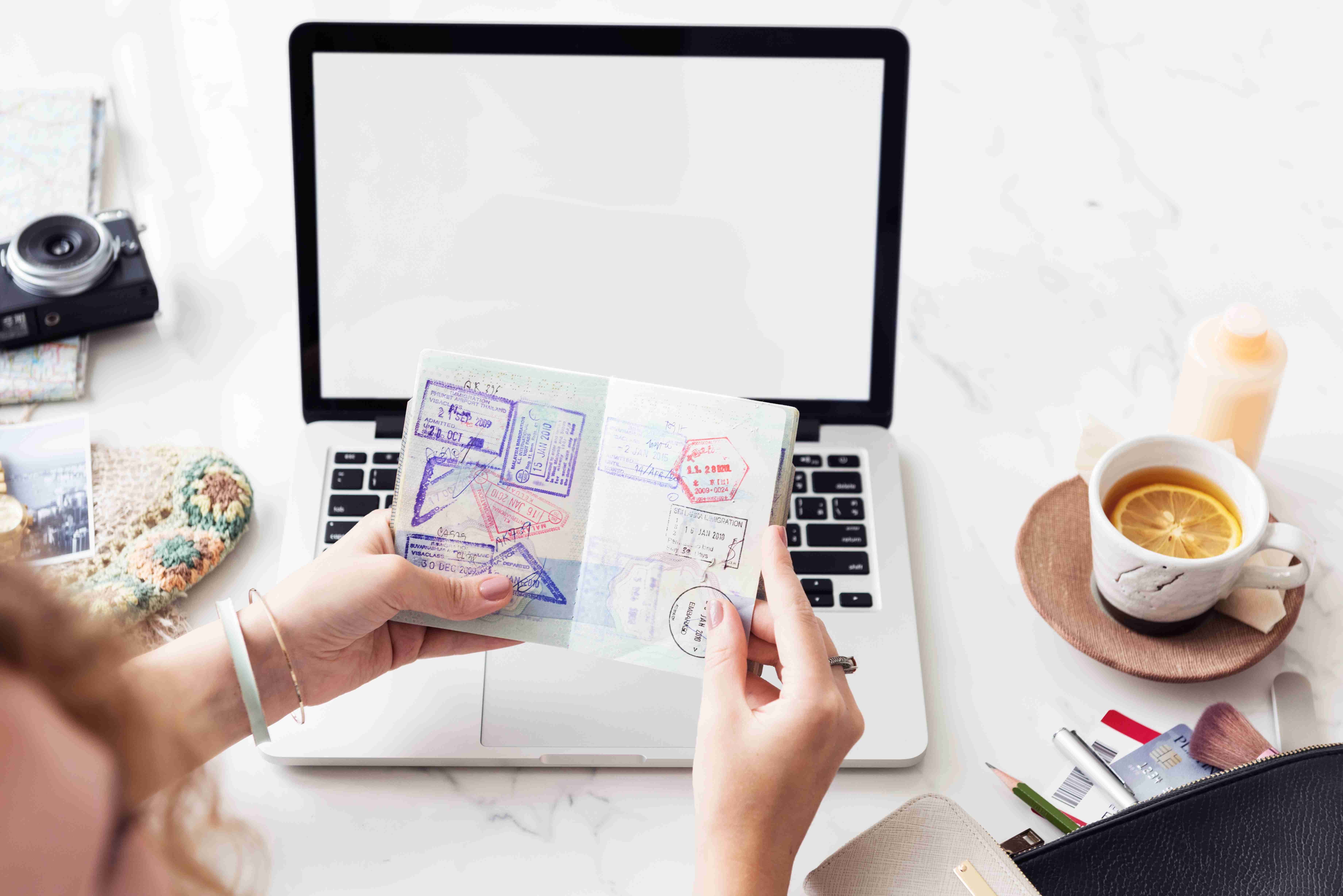 Handholding passport with visa stamps and laptop